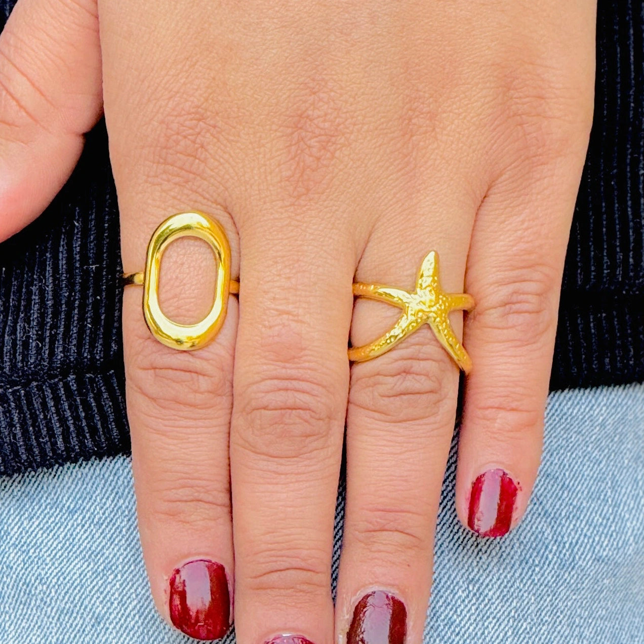 Gold ring with a star design on a finger with red nail polish.