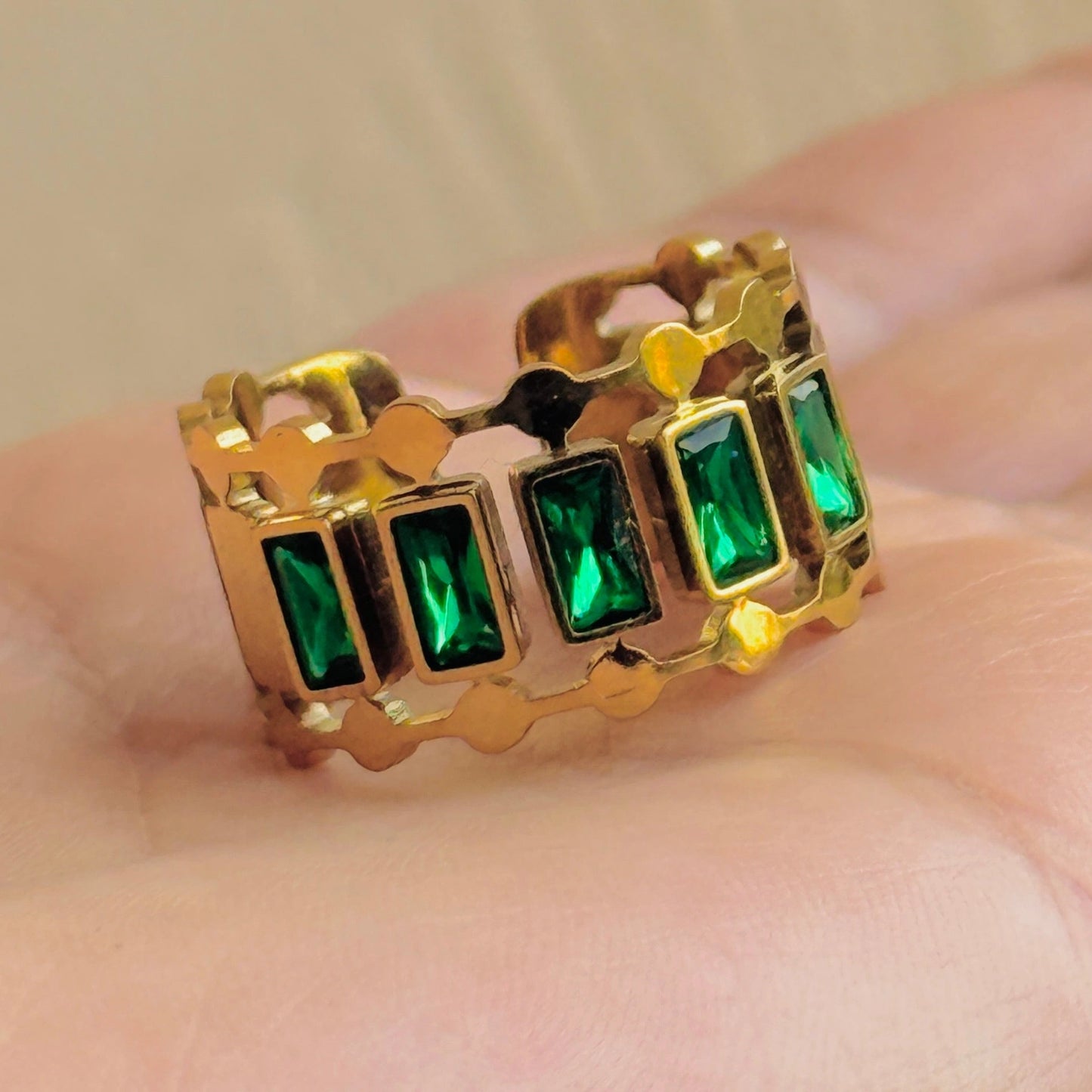 Gold ring with green gemstones on a hand