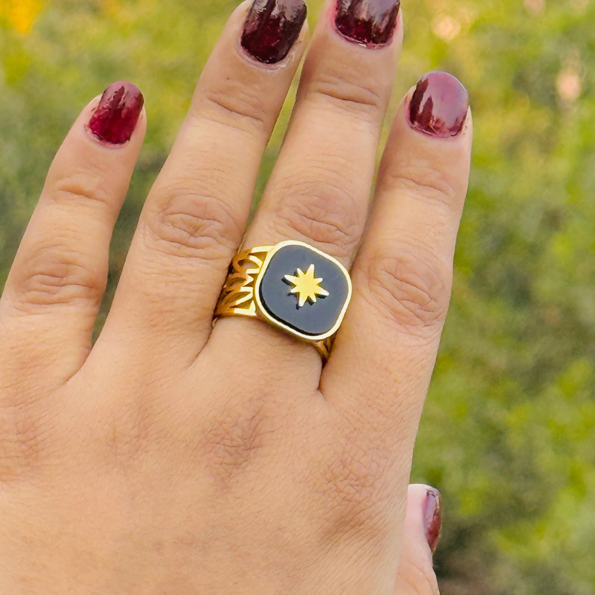 Gold ring with a blue stone and star design on a person's finger against a blurred green background