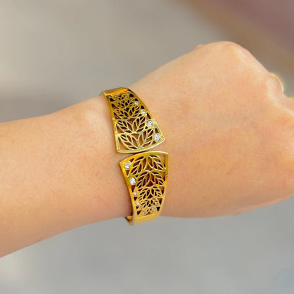 Gold bracelet with intricate design on a wrist against a neutral background