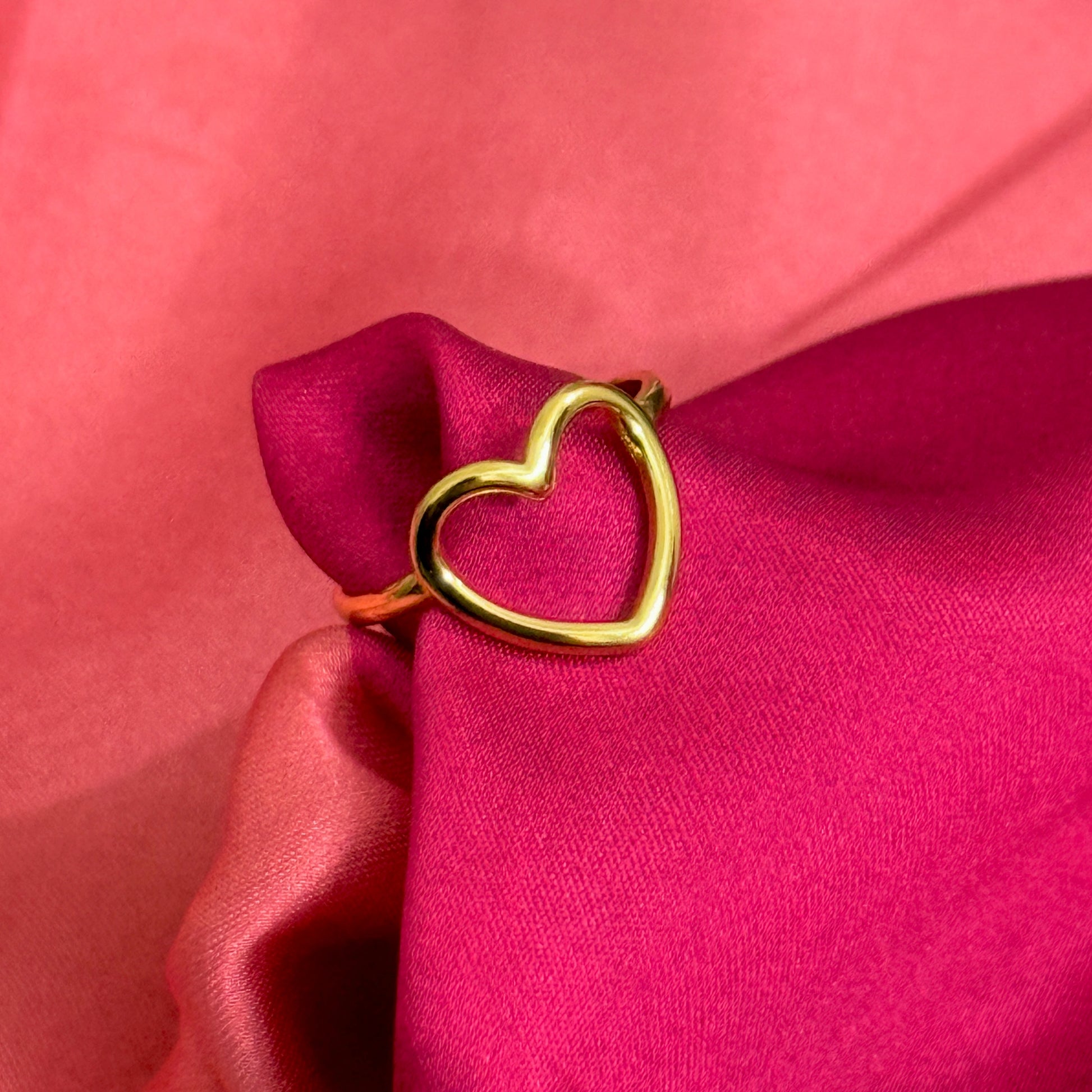 Gold heart-shaped ring on a pink fabric background