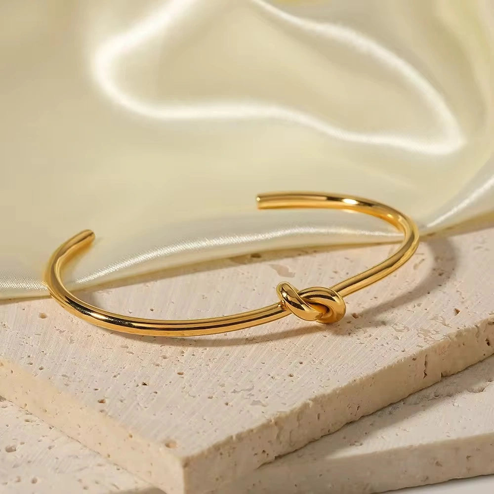 Gold bracelet with knot design on a beige fabric background