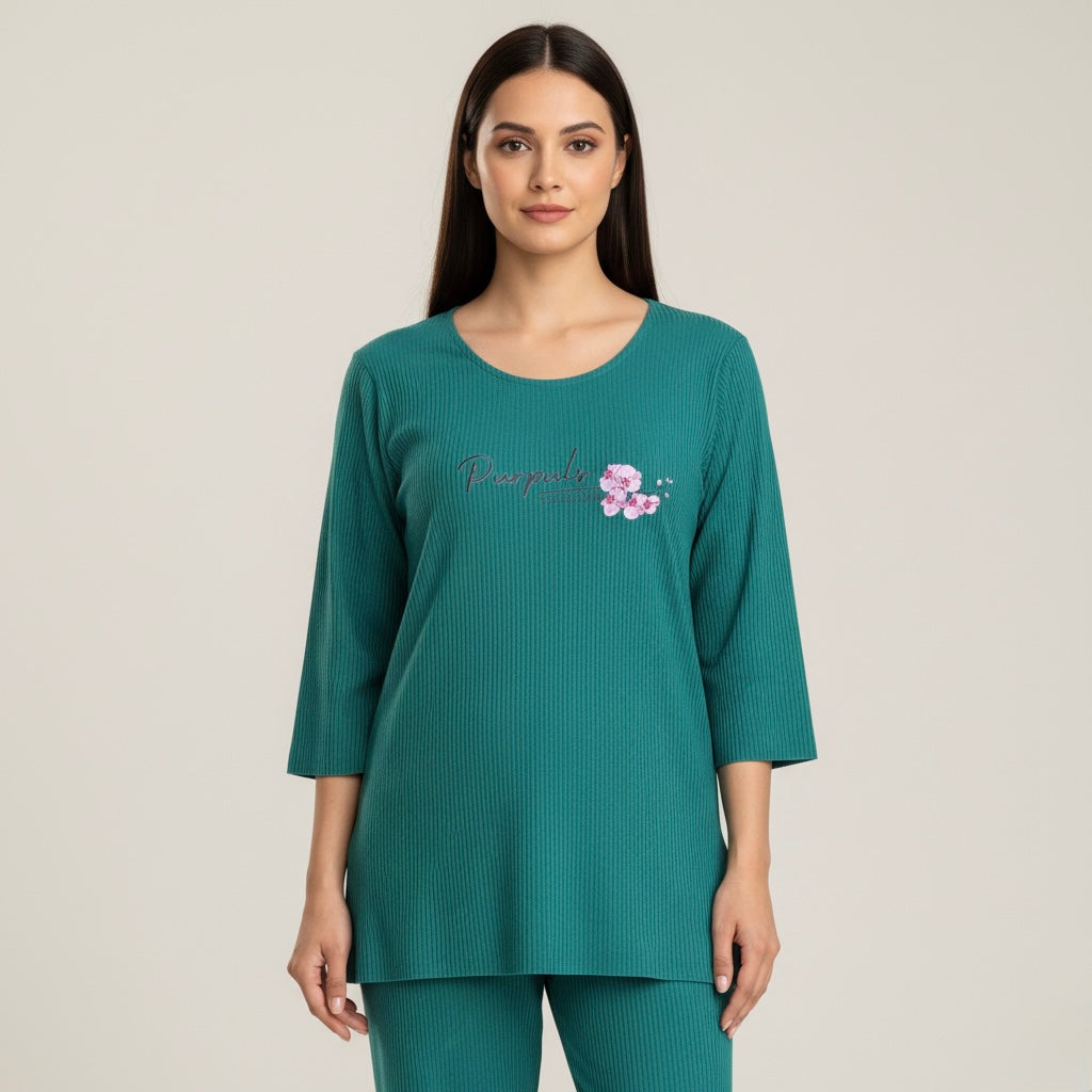 Woman wearing a teal ribbed top with floral design and text on a plain background