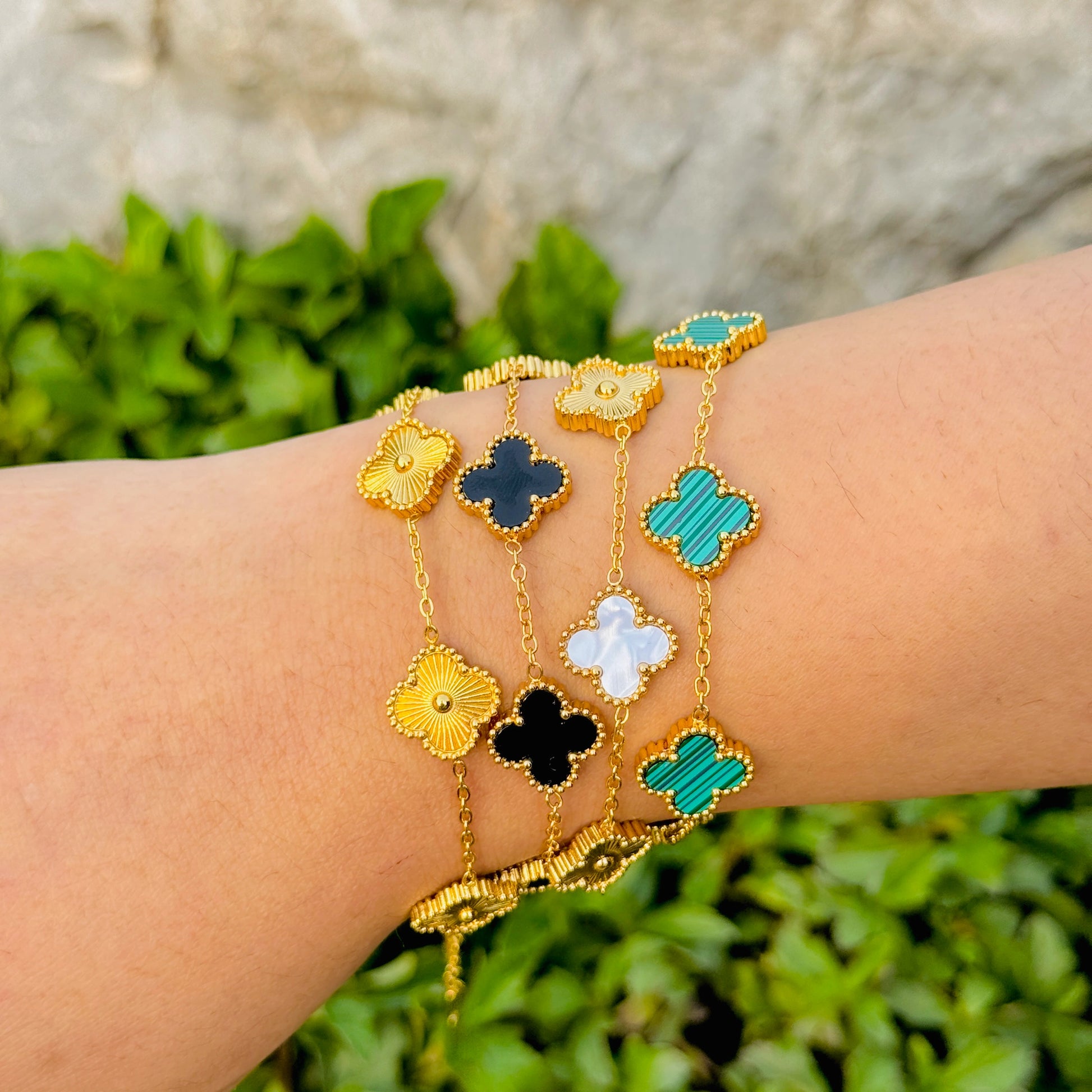 Wrist wearing multiple gold bracelets with colorful clover-shaped charms against a natural background