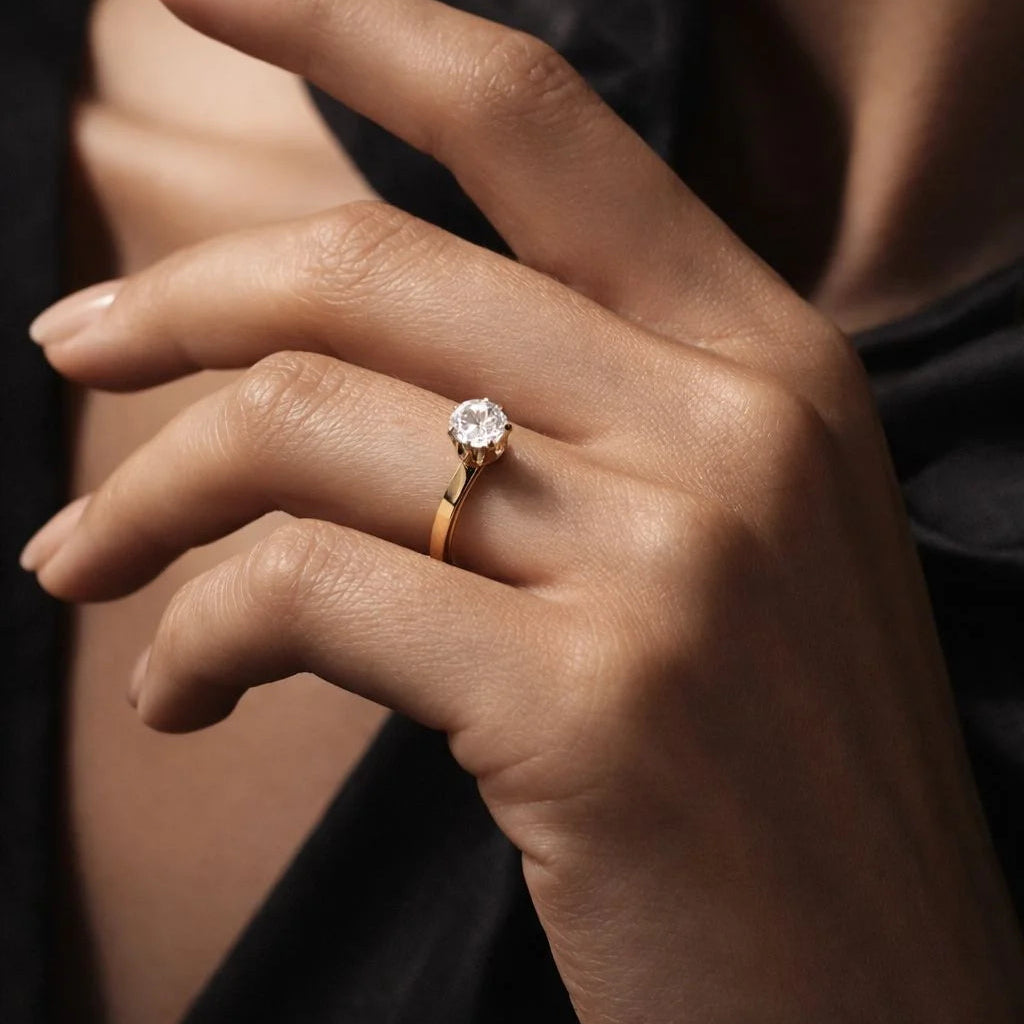 Hand wearing a gold ring with a diamond on a dark background