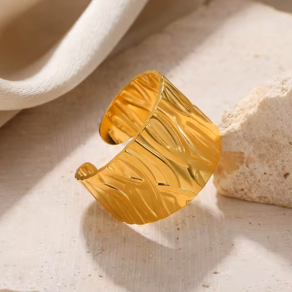 Gold cuff bracelet on a textured beige surface