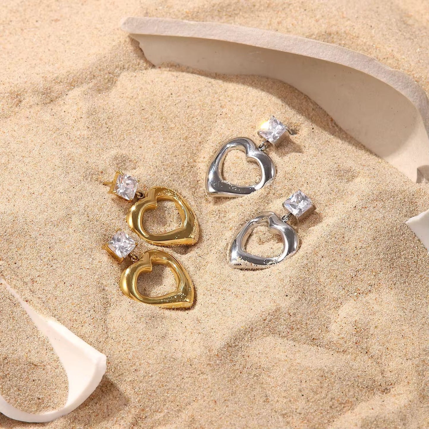 Heart-shaped earrings with gemstones on a sandy surface