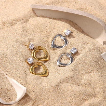 Heart-shaped earrings with gemstones on a sandy surface