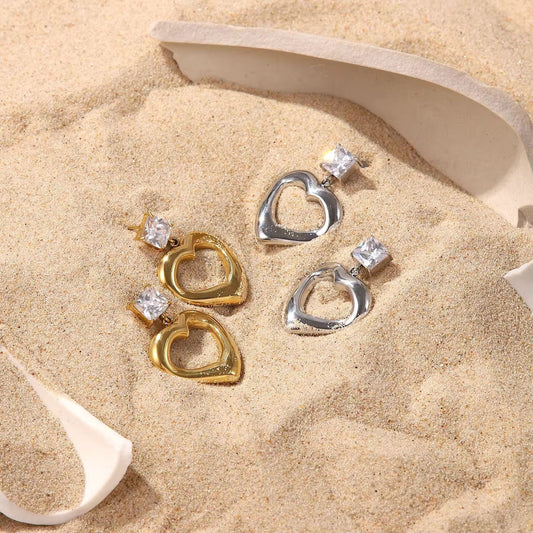 Heart-shaped earrings with gemstones on a sandy surface
