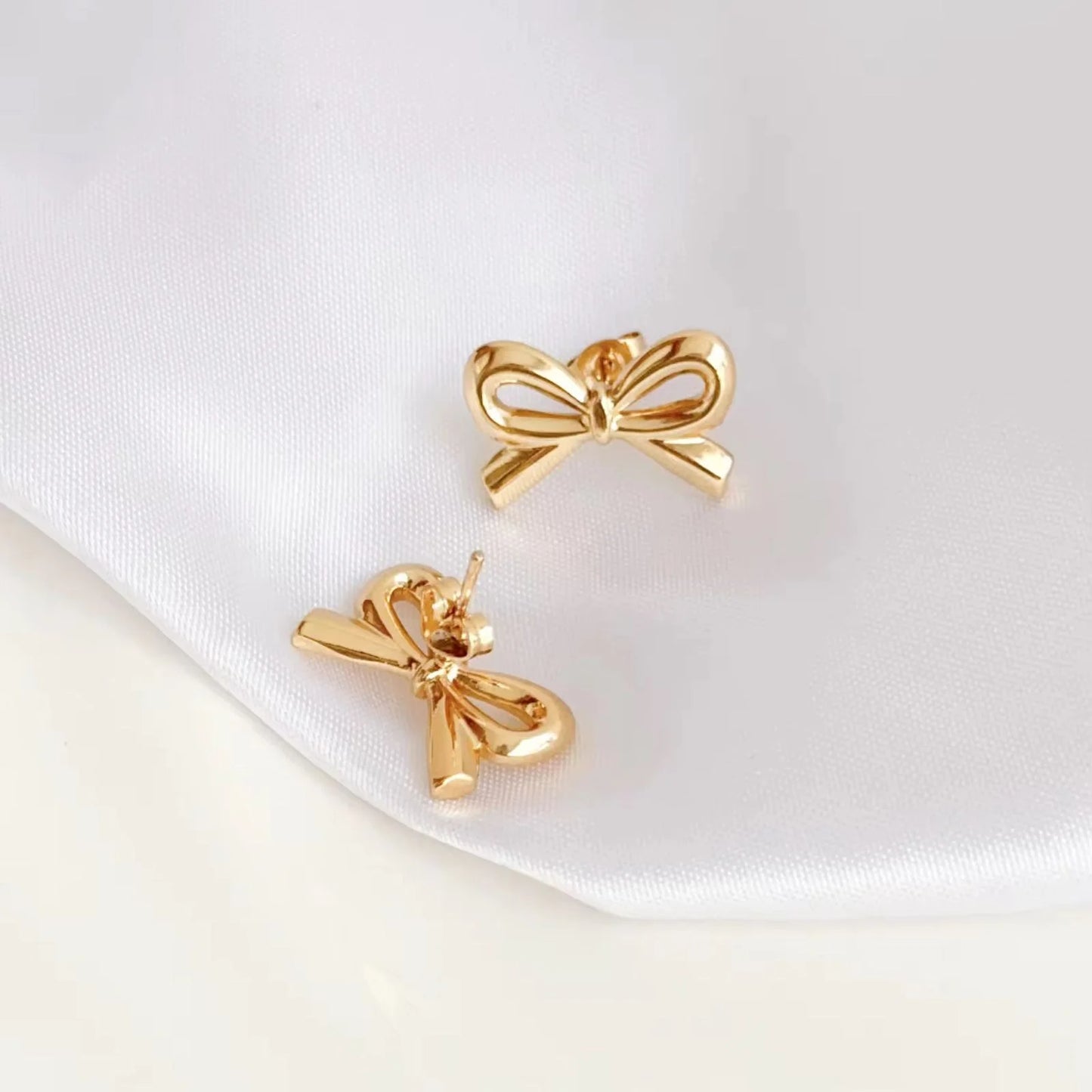 Gold bow-shaped earrings on a white satin background