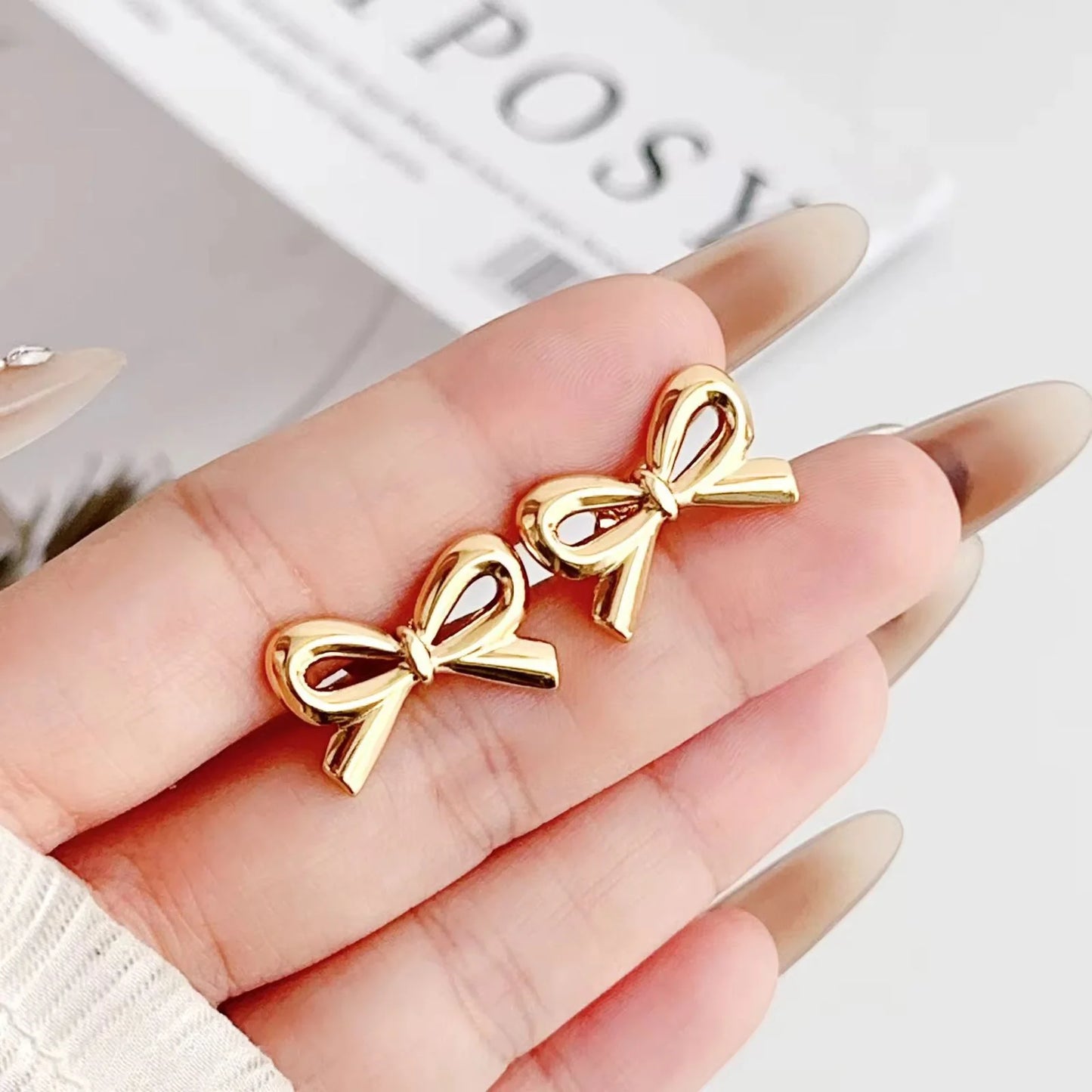 Gold bow-shaped earrings held in a hand with a blurred background