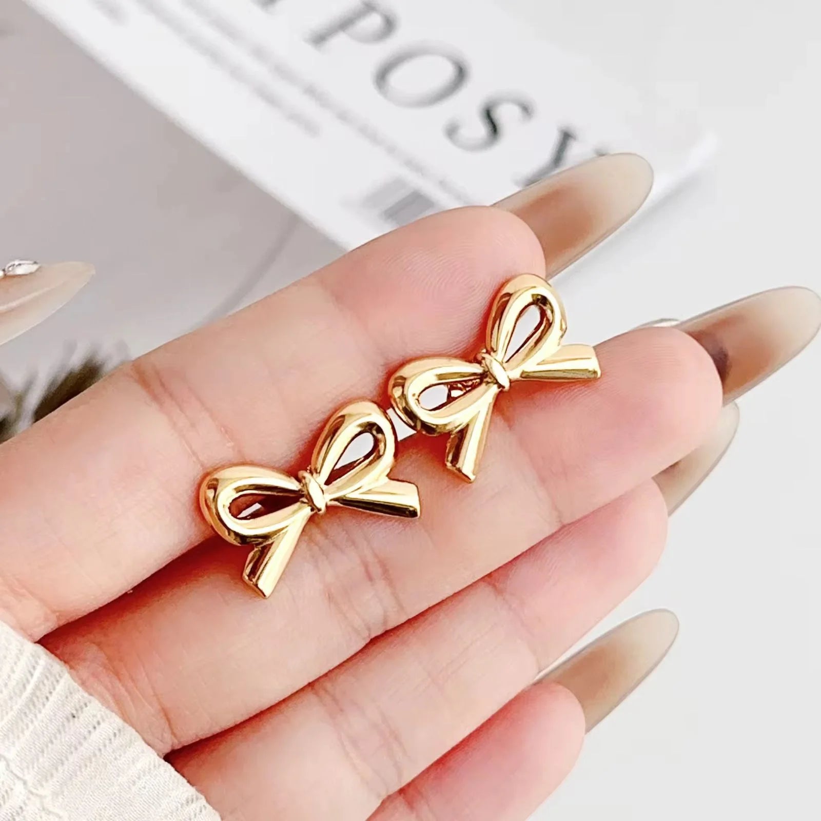 Gold bow-shaped earrings held in a hand with a blurred background