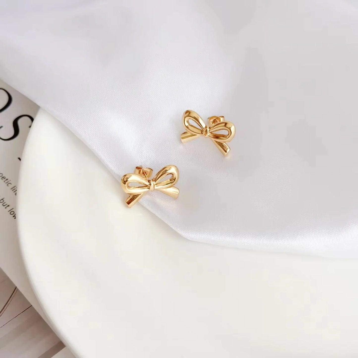 Gold bow-shaped earrings on a white surface