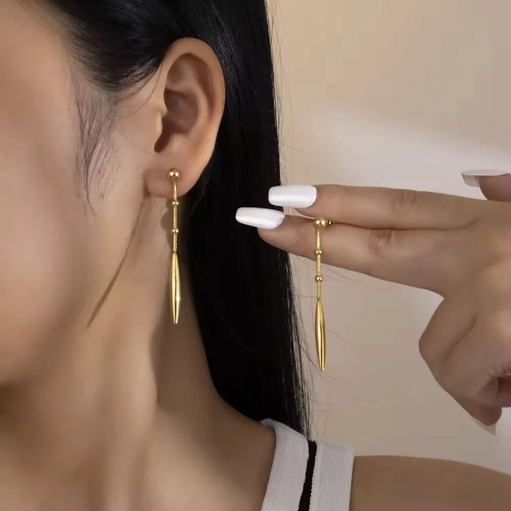 Gold earrings being worn and held by a hand against a neutral background