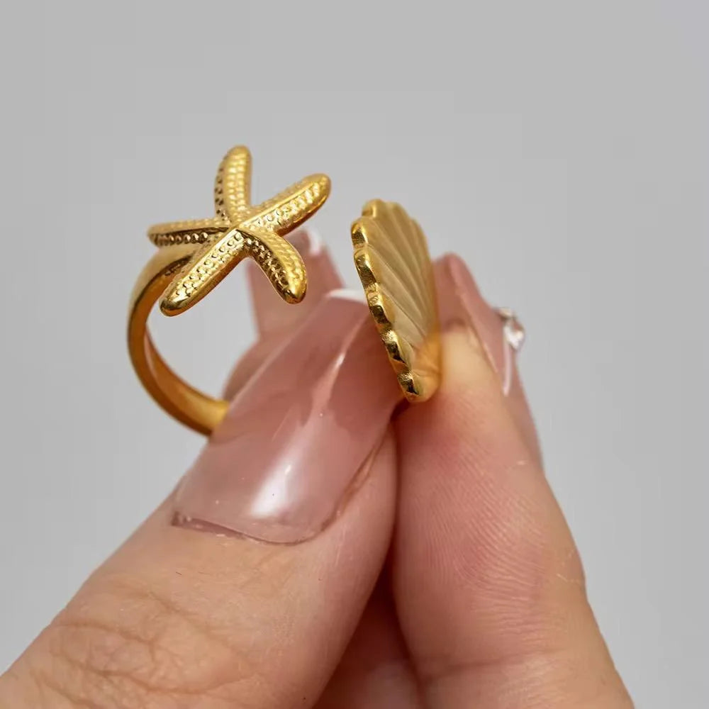Gold starfish-shaped ring on a hand against a gray background