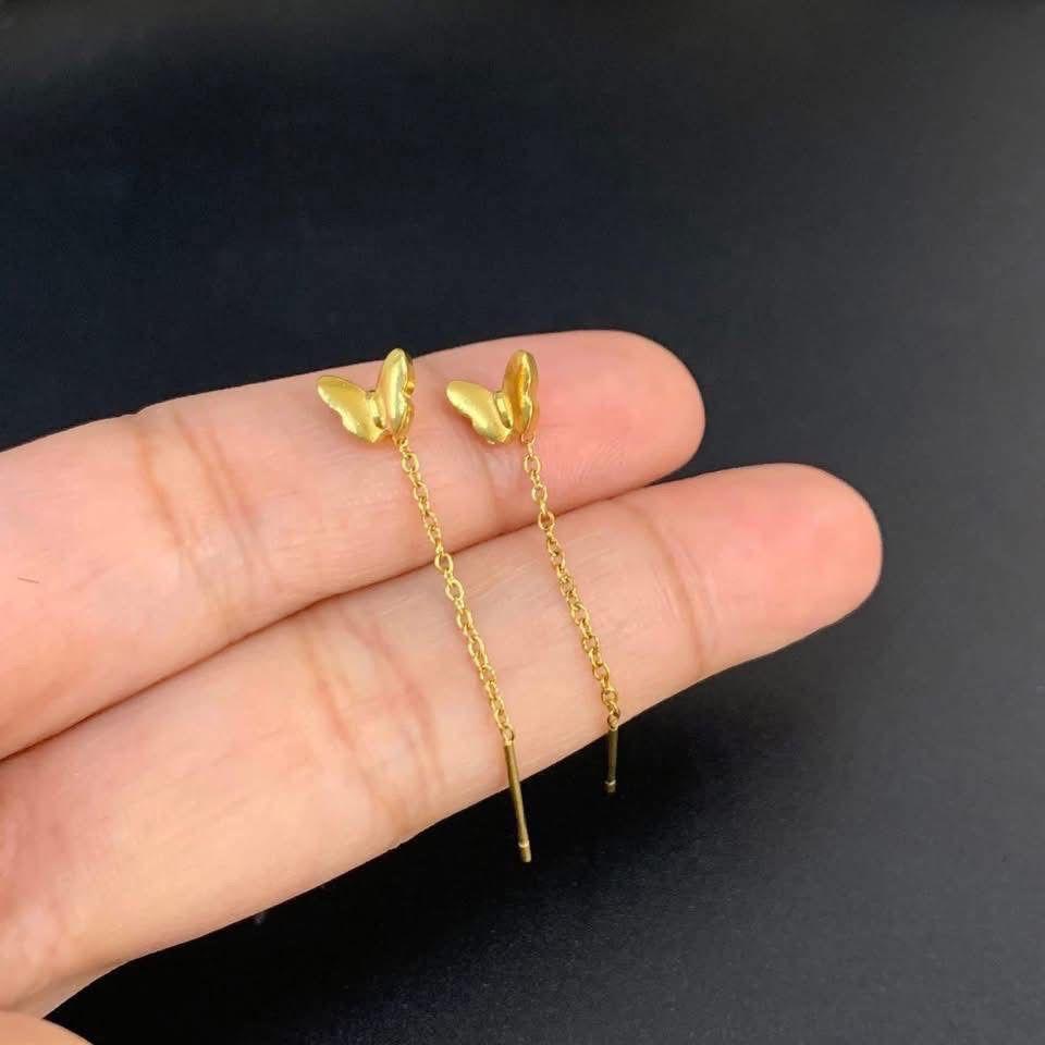 Gold butterfly earrings held between fingers against a dark background