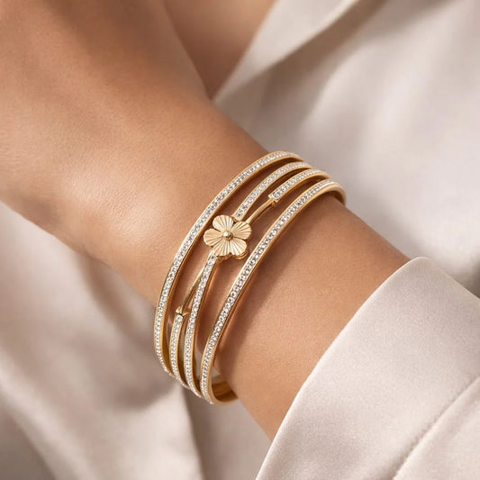Gold bracelet with floral design on a wrist against a neutral background