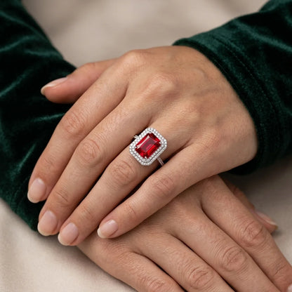 Close-up of a hand wearing a ring with a red gemstone on a neutral background