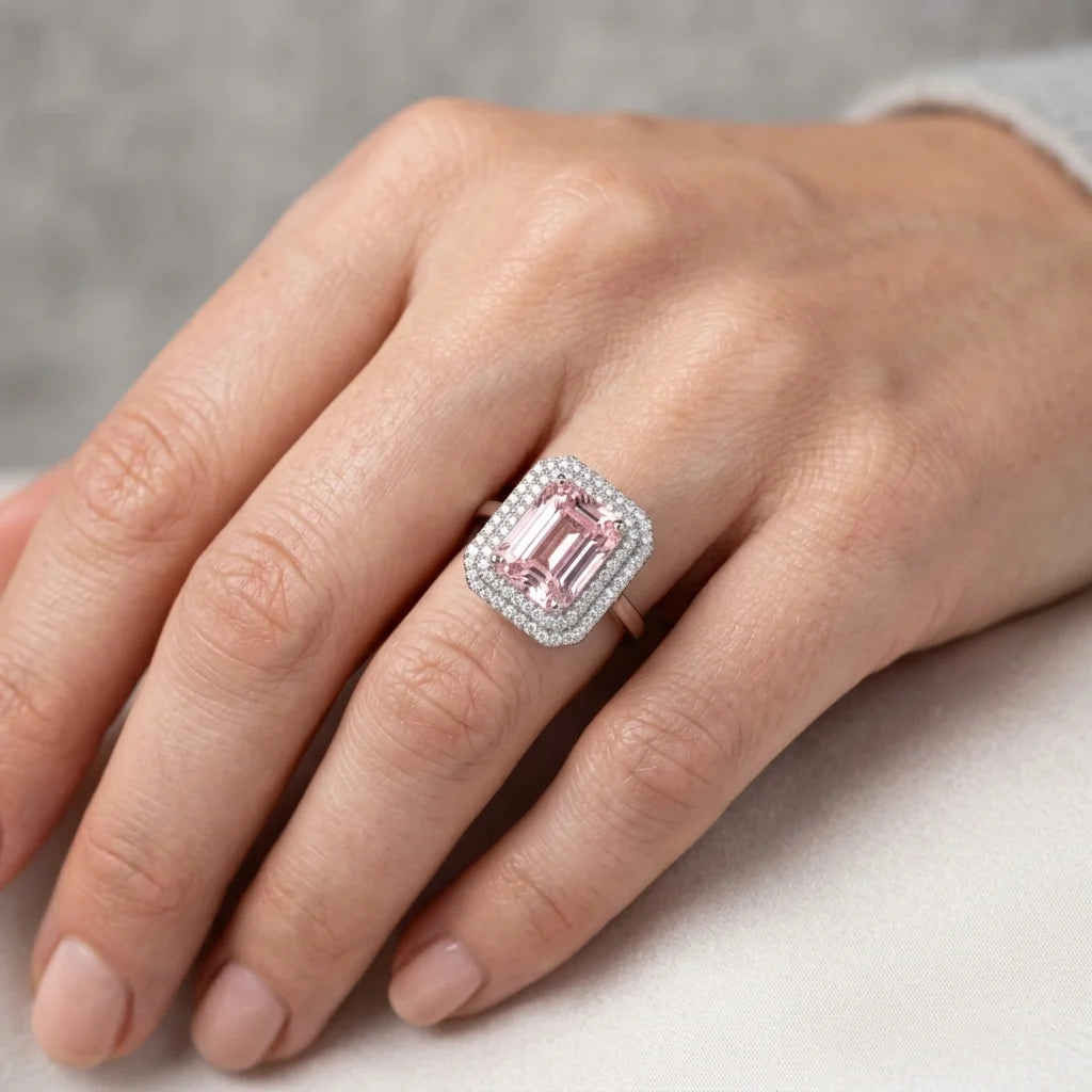 Pink gemstone ring with diamond accents on a hand against a neutral background
