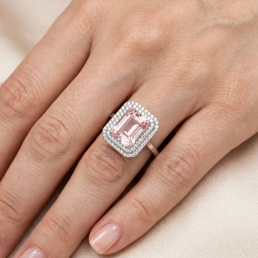 Ring with a pink gemstone on a hand against a beige background