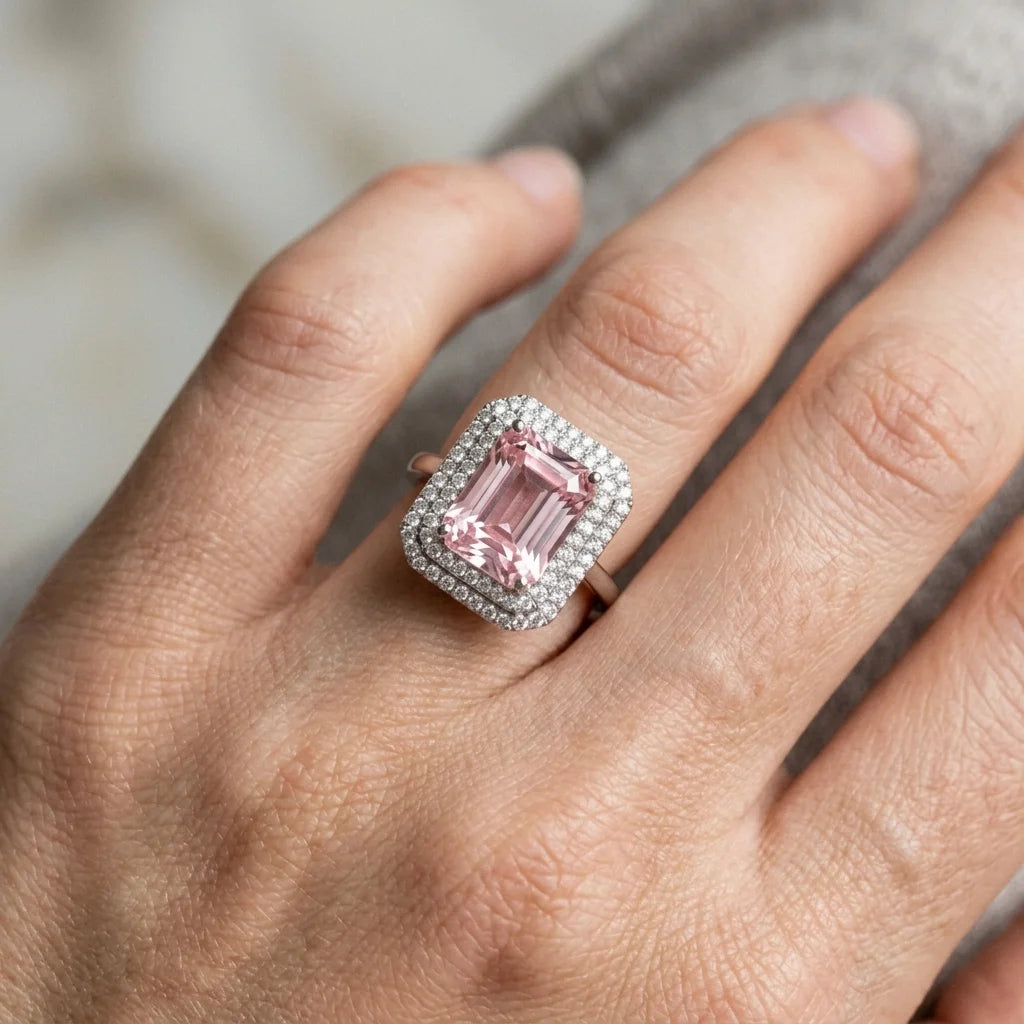 Hand wearing a ring with a pink gemstone and diamond accents.