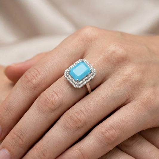 Ring with a blue gemstone on a person's finger against a neutral background
