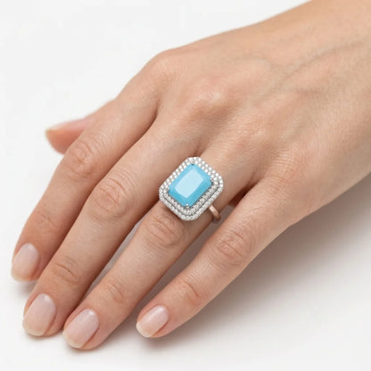 Hand wearing a ring with a blue gemstone on a white background