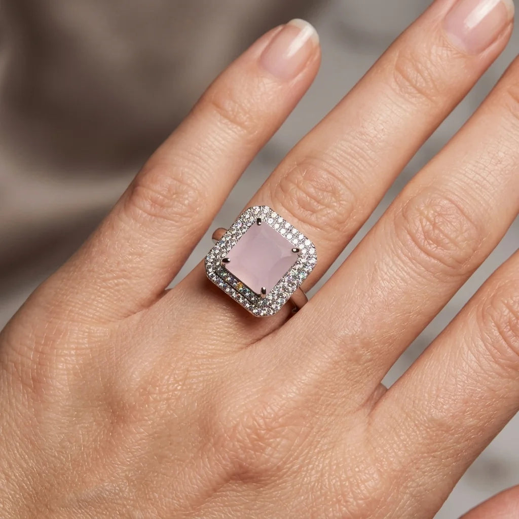 Hand wearing a ring with a pink stone and diamond accents on a neutral background