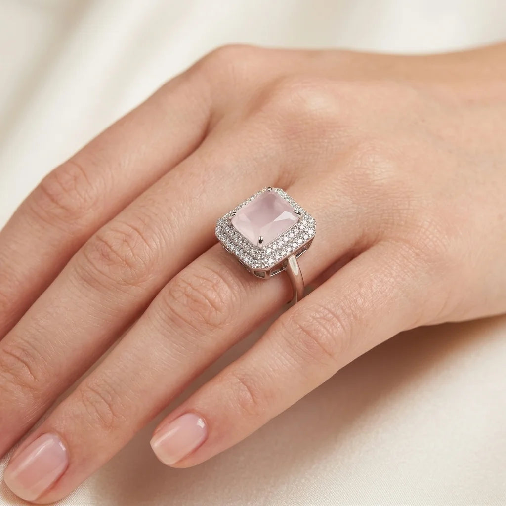 Ring with a pink gemstone on a hand against a neutral background