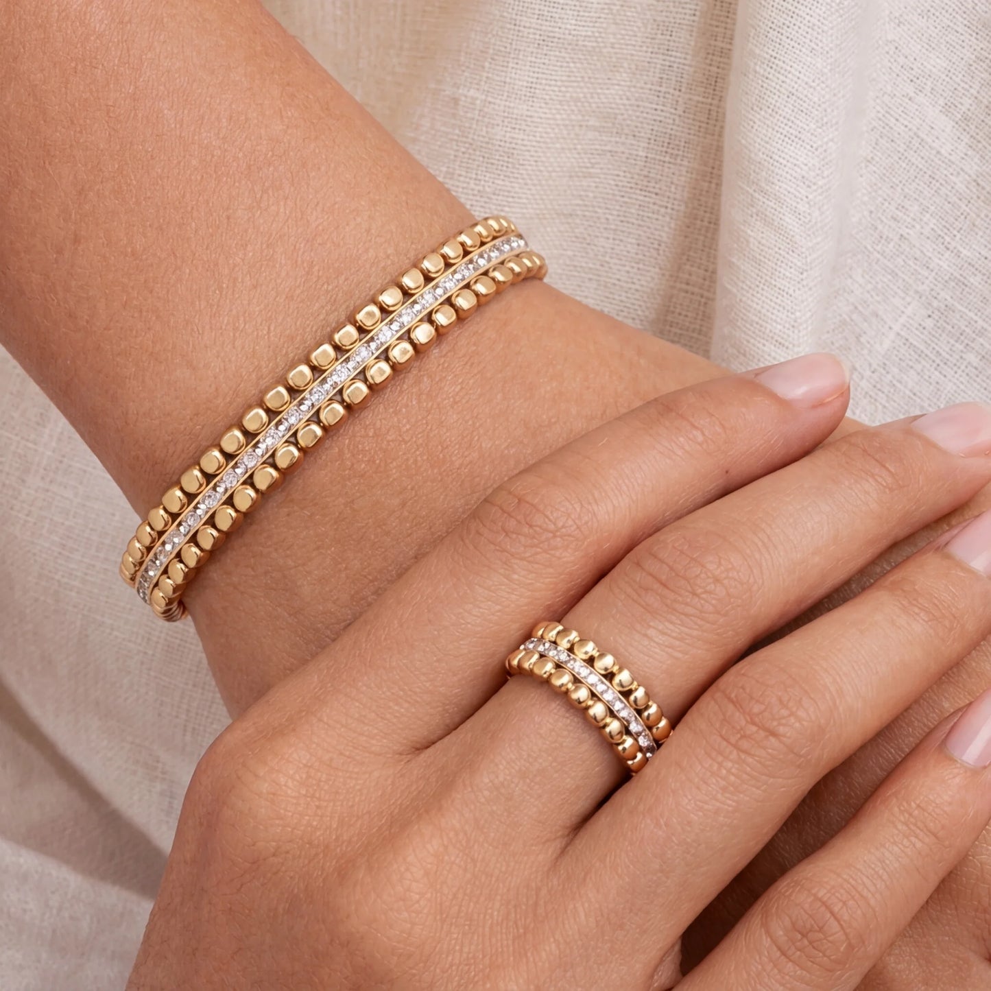Gold bracelet and ring on a hand against a neutral background