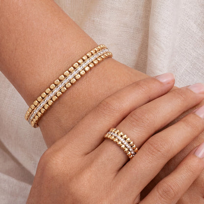 Gold bracelet and ring on a hand against a neutral background