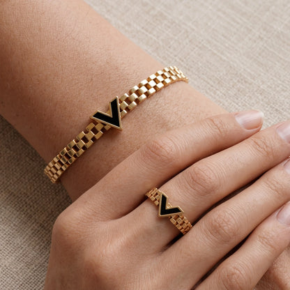 Gold bracelet and ring with black chevron design on a beige background