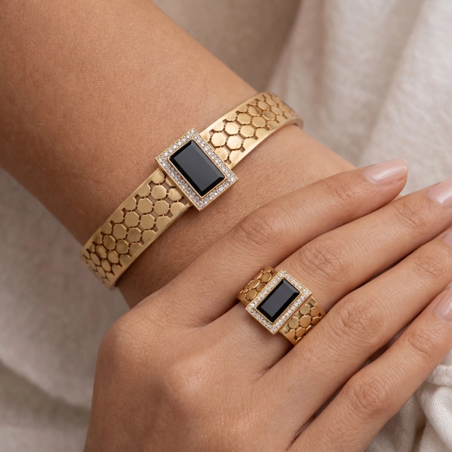 Gold bracelet and ring with black gemstones on a neutral background