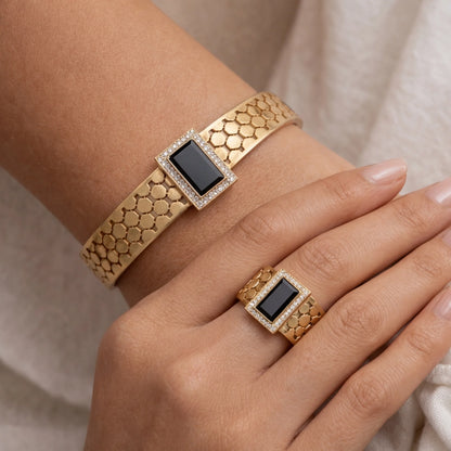 Gold bracelet and ring with black gemstones on a neutral background