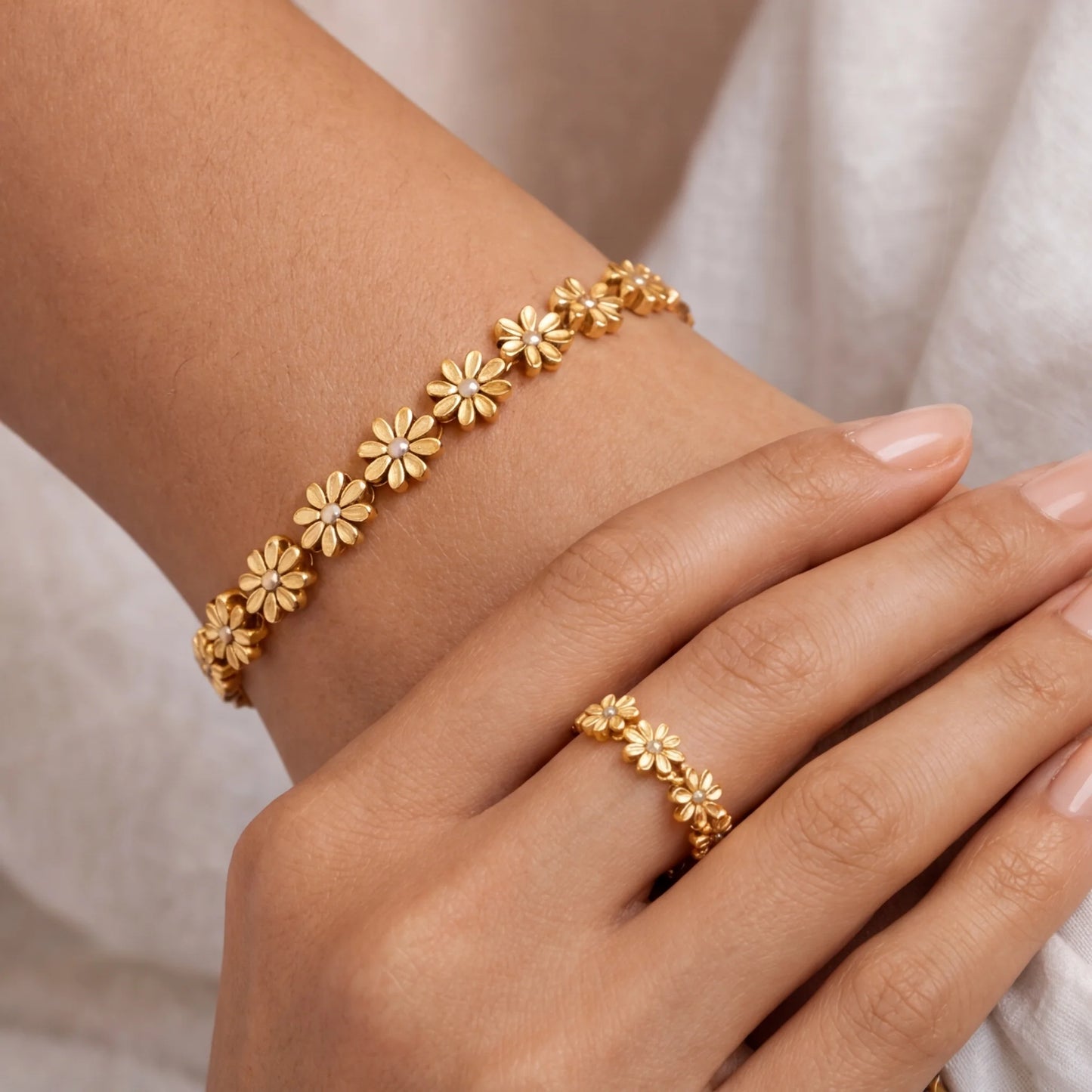 Gold bracelet and ring on a hand against a neutral background