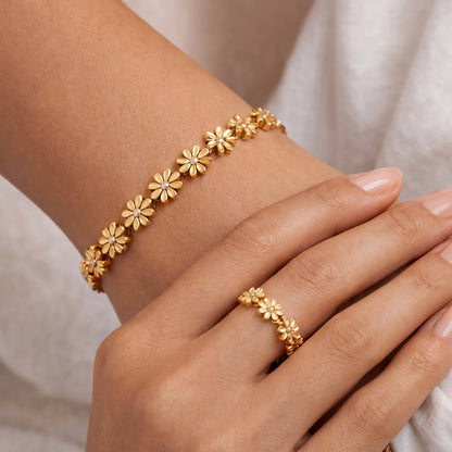 Gold bracelet and ring on a hand against a neutral background