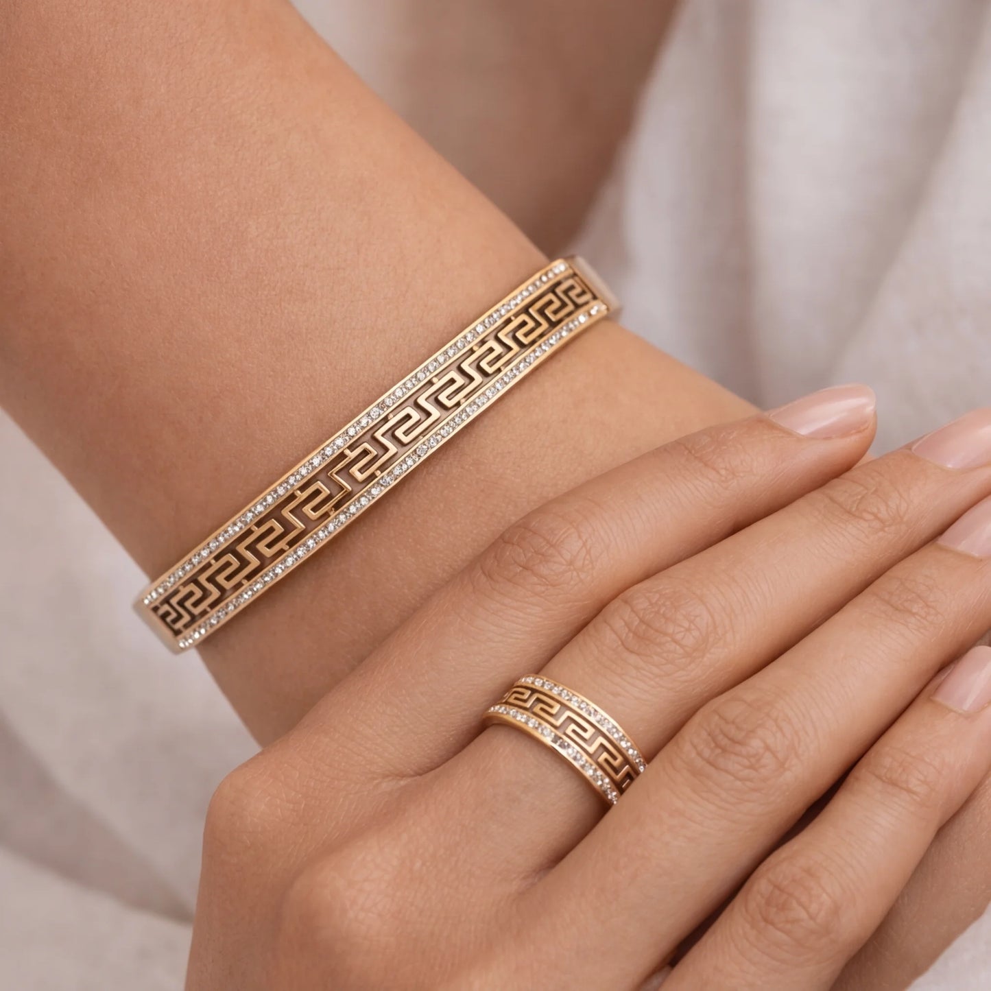 Gold bracelet and ring on a wrist with a neutral background