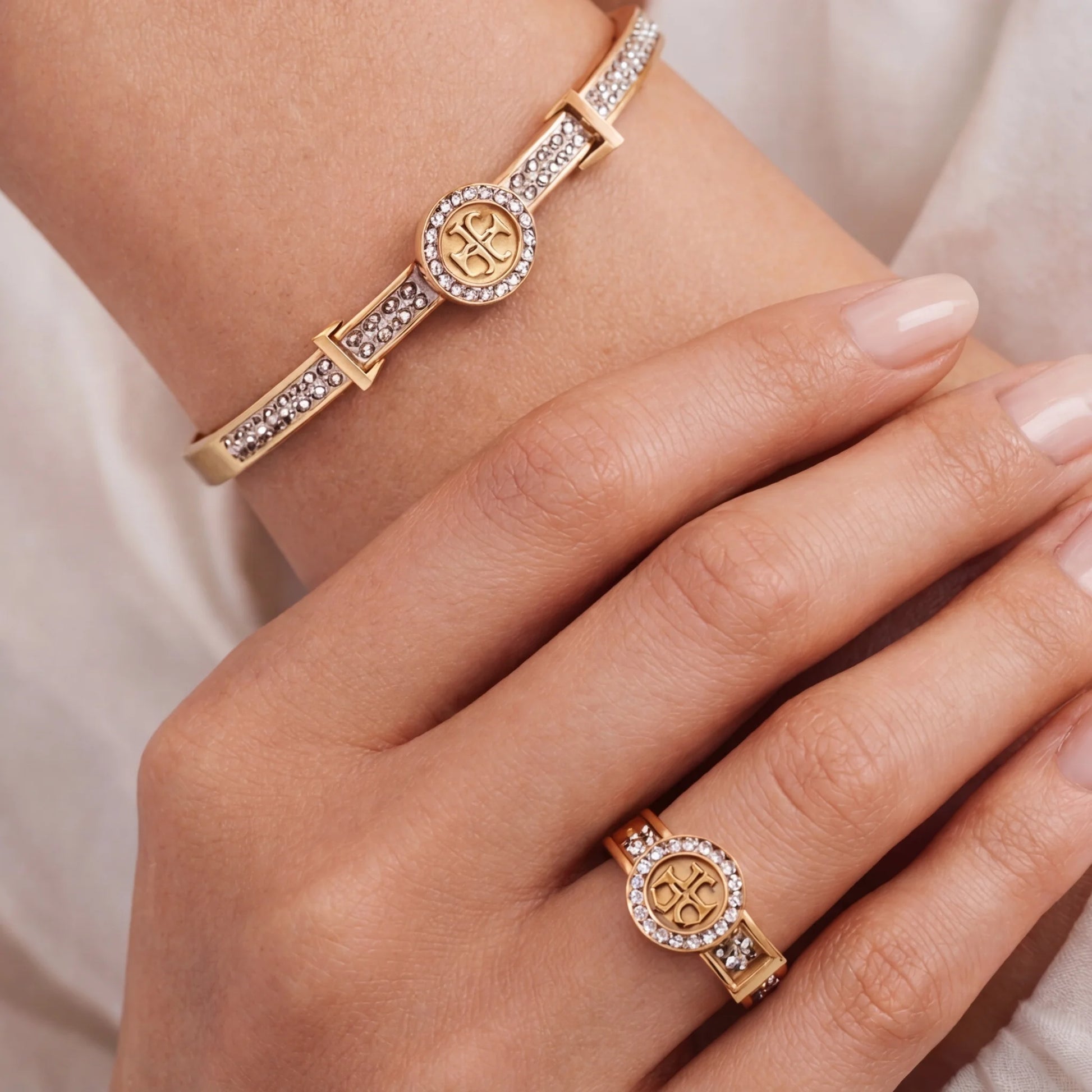 Gold bracelet and ring with gemstones on a hand against a neutral background