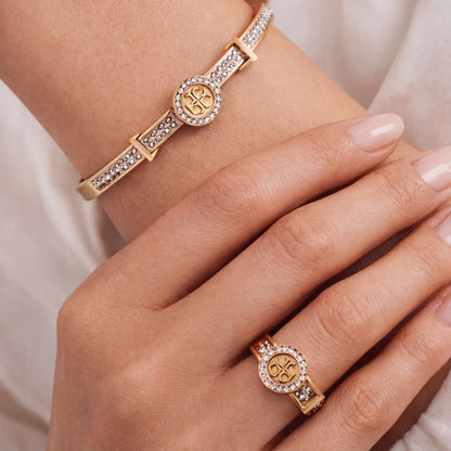 Gold bracelet and ring with gemstones on a hand against a neutral background