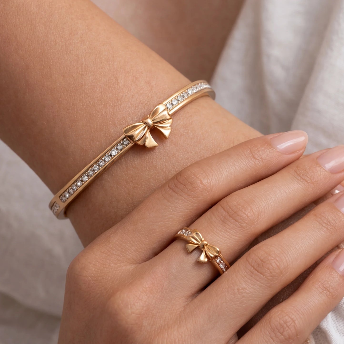 Gold bracelet and ring with bow design on a wrist against a neutral background