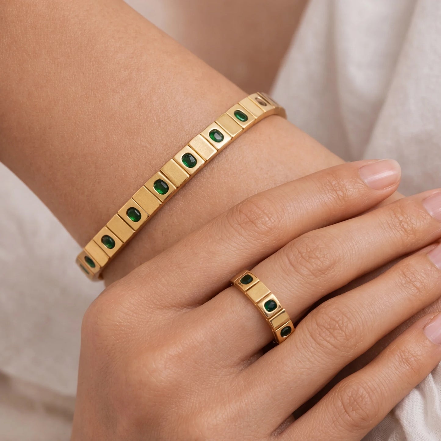 Gold bracelet and ring with green gemstones on a wrist and hand.