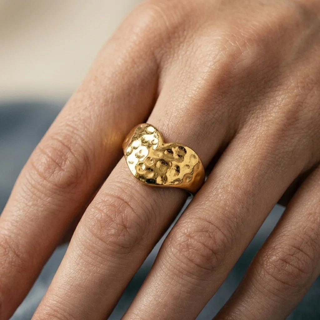 Gold heart-shaped ring on a finger with a blurred background