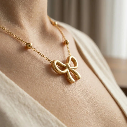 Gold bow-shaped necklace on a person's neck with a neutral background