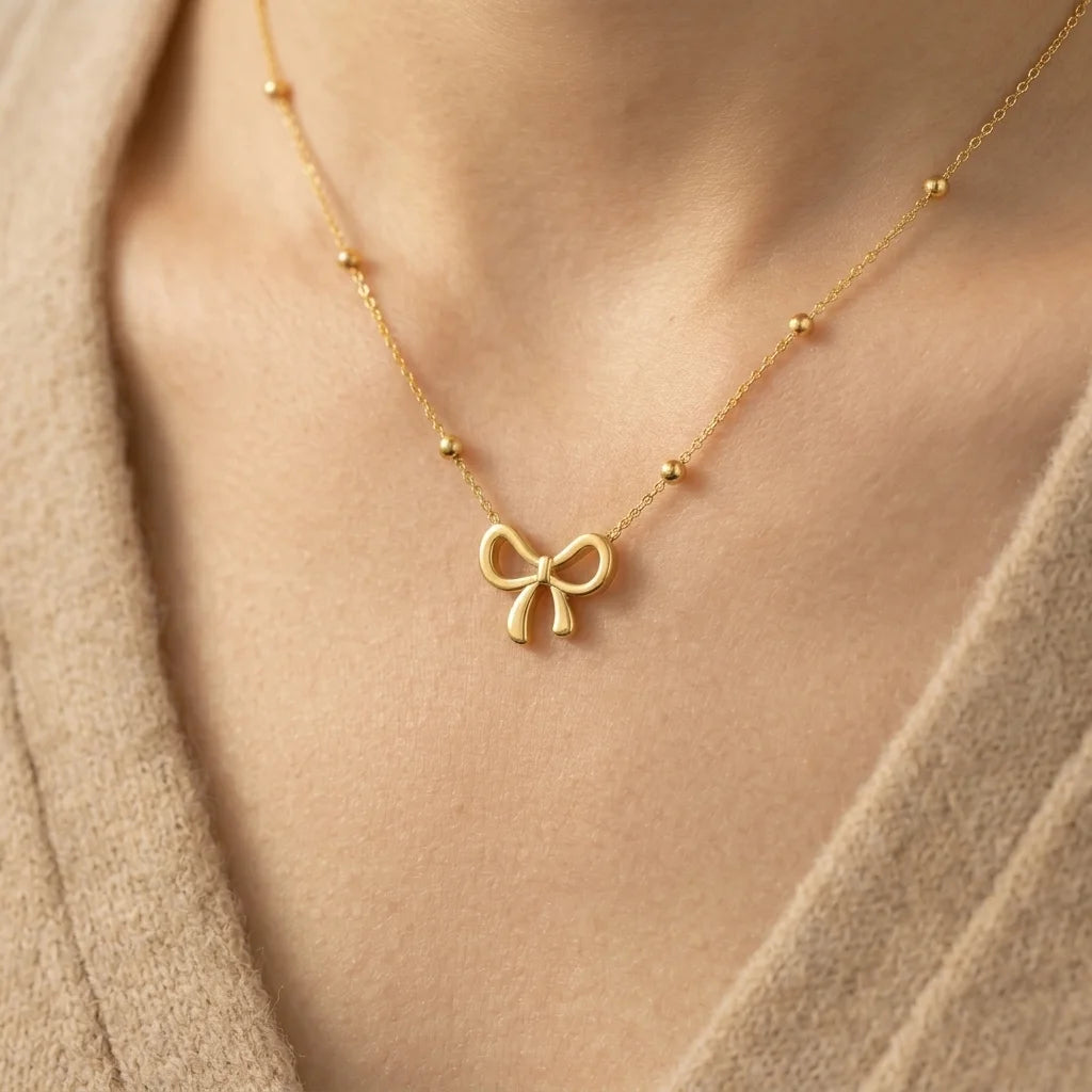 Gold necklace with a bow pendant on a person wearing a beige sweater.