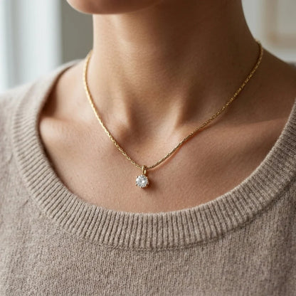 Gold necklace with a diamond pendant worn by a person in a beige sweater.