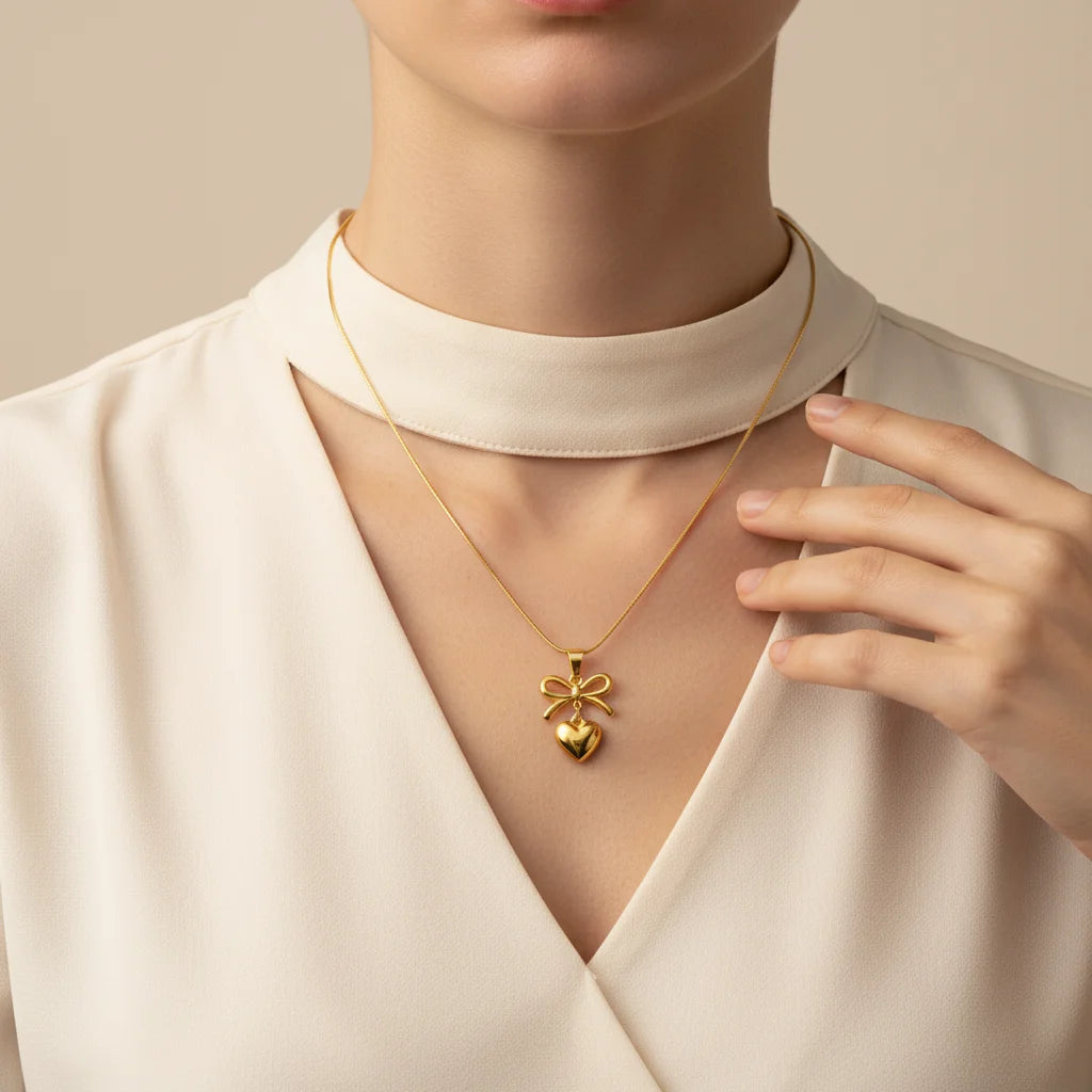 Gold necklace with a bow pendant worn by a person in a white outfit.