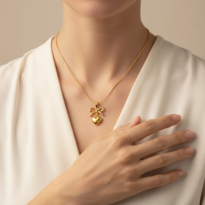 Gold necklace with a heart and bow pendant worn by a person in a white outfit.