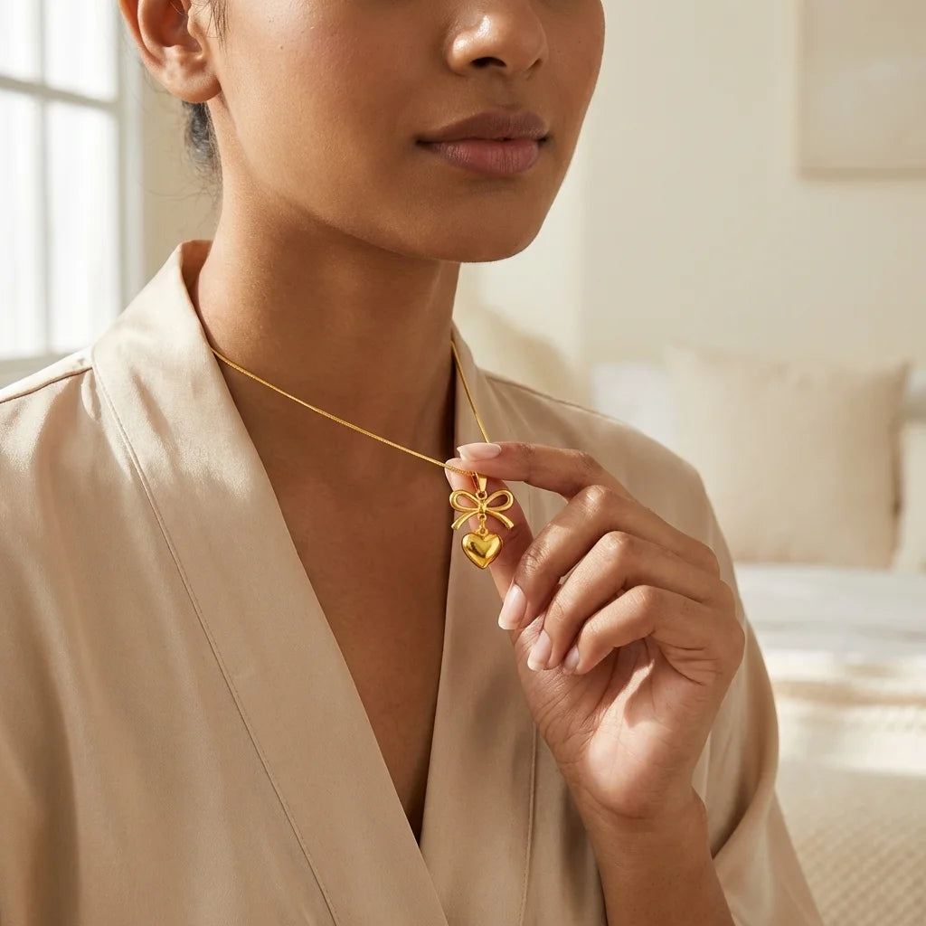 Woman wearing a gold necklace with a heart-shaped pendant in a softly lit room.