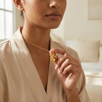Woman wearing a gold necklace with a heart-shaped pendant in a softly lit room.