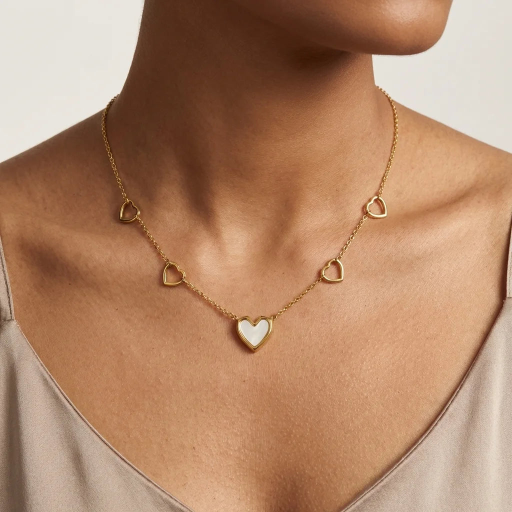 Gold necklace with heart-shaped pendants on a person wearing a beige top.